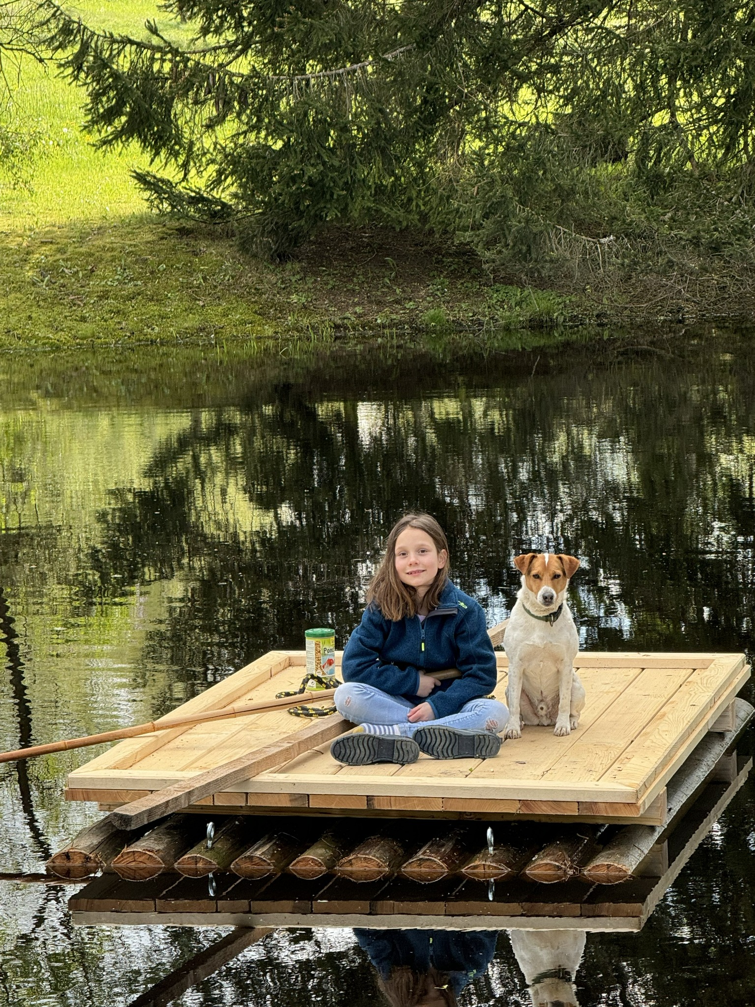 Kind mit Hund auf einem Floß am Teich